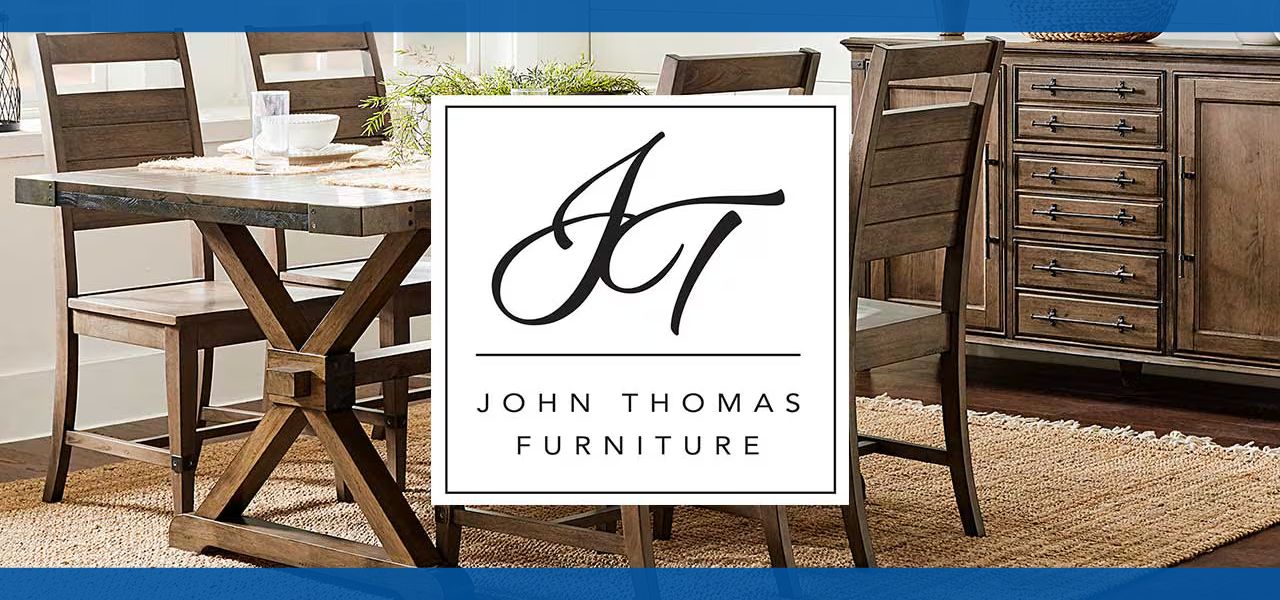 Logo of John Thomas Furniture with a wooden dining setup.