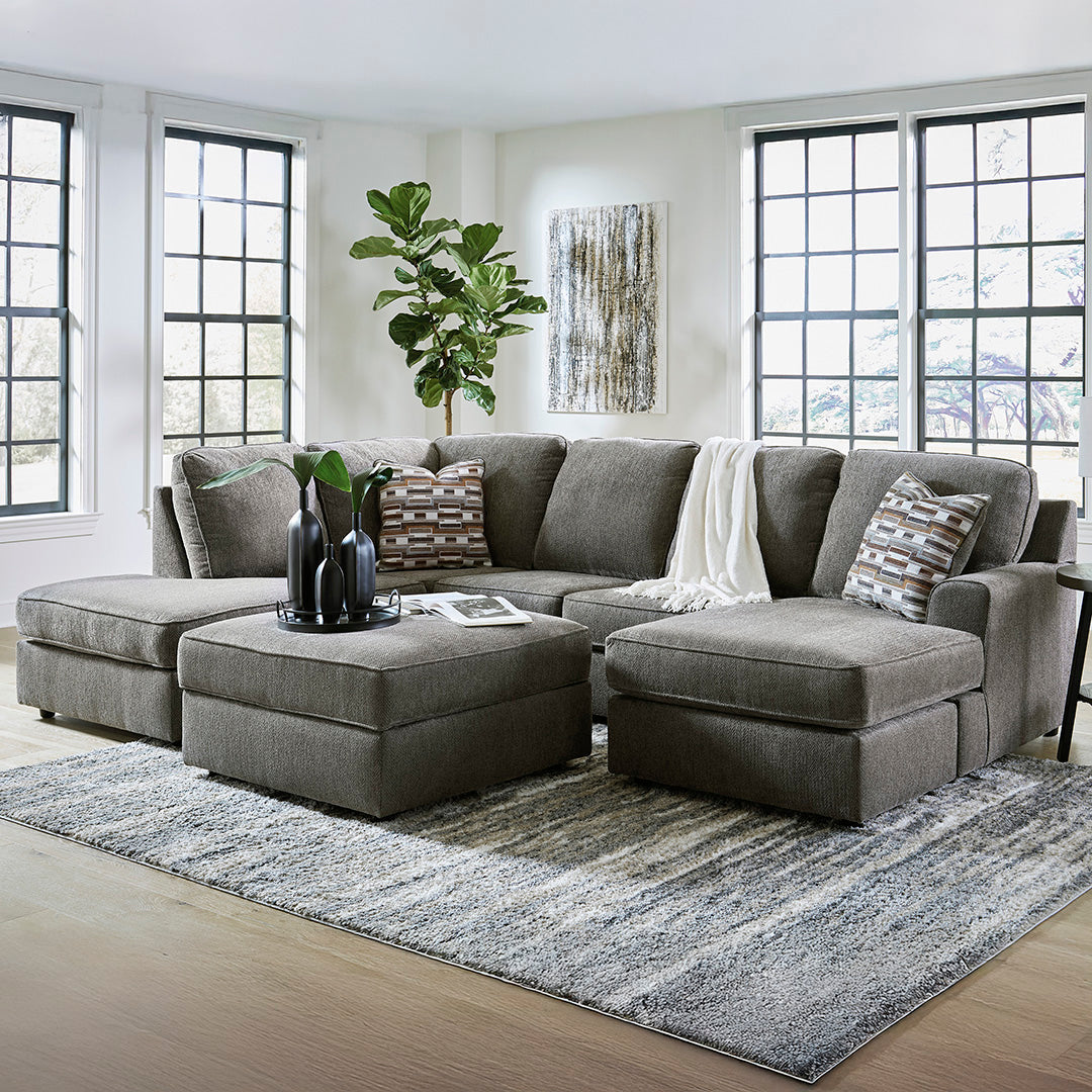 Gray sectional sofa in a living room with a rug, plants, and artwork.