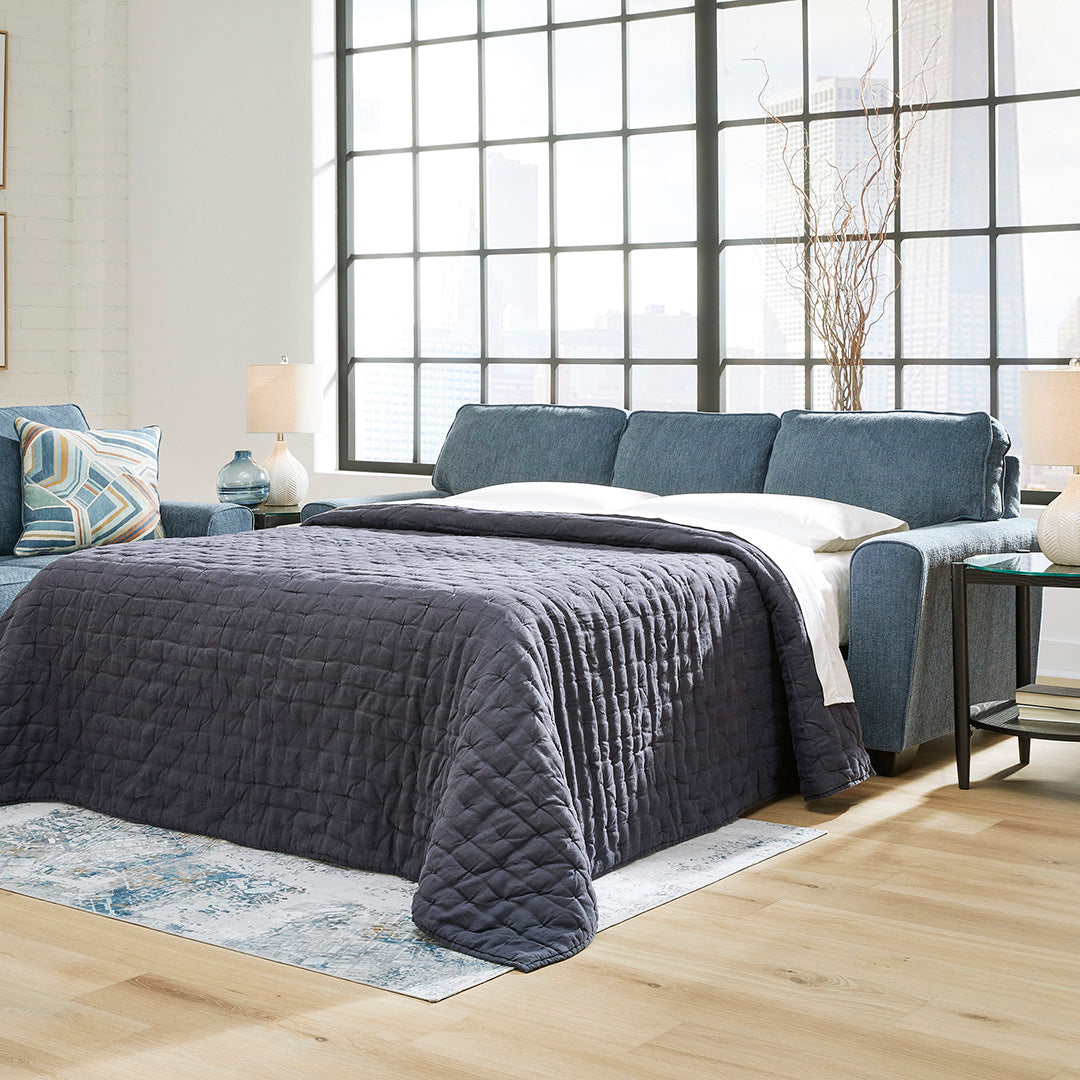 Modern sofa bed by Ashley Furniture with a gray quilted cover on a bed, large window, and side tables.