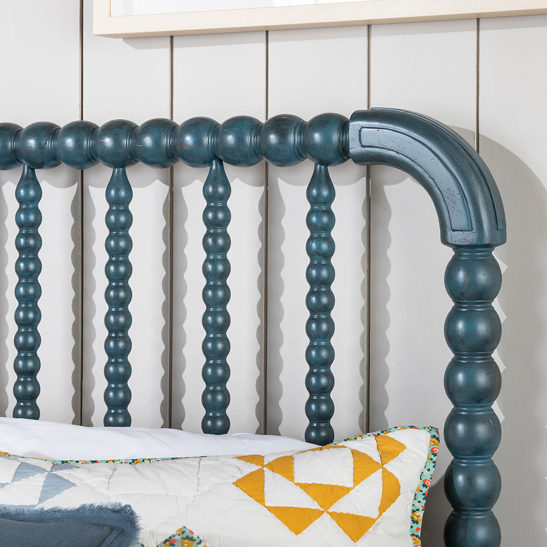 Close-up of a painted wooden bed frame headboard with turned spindle-style posts and a curved upper rail.