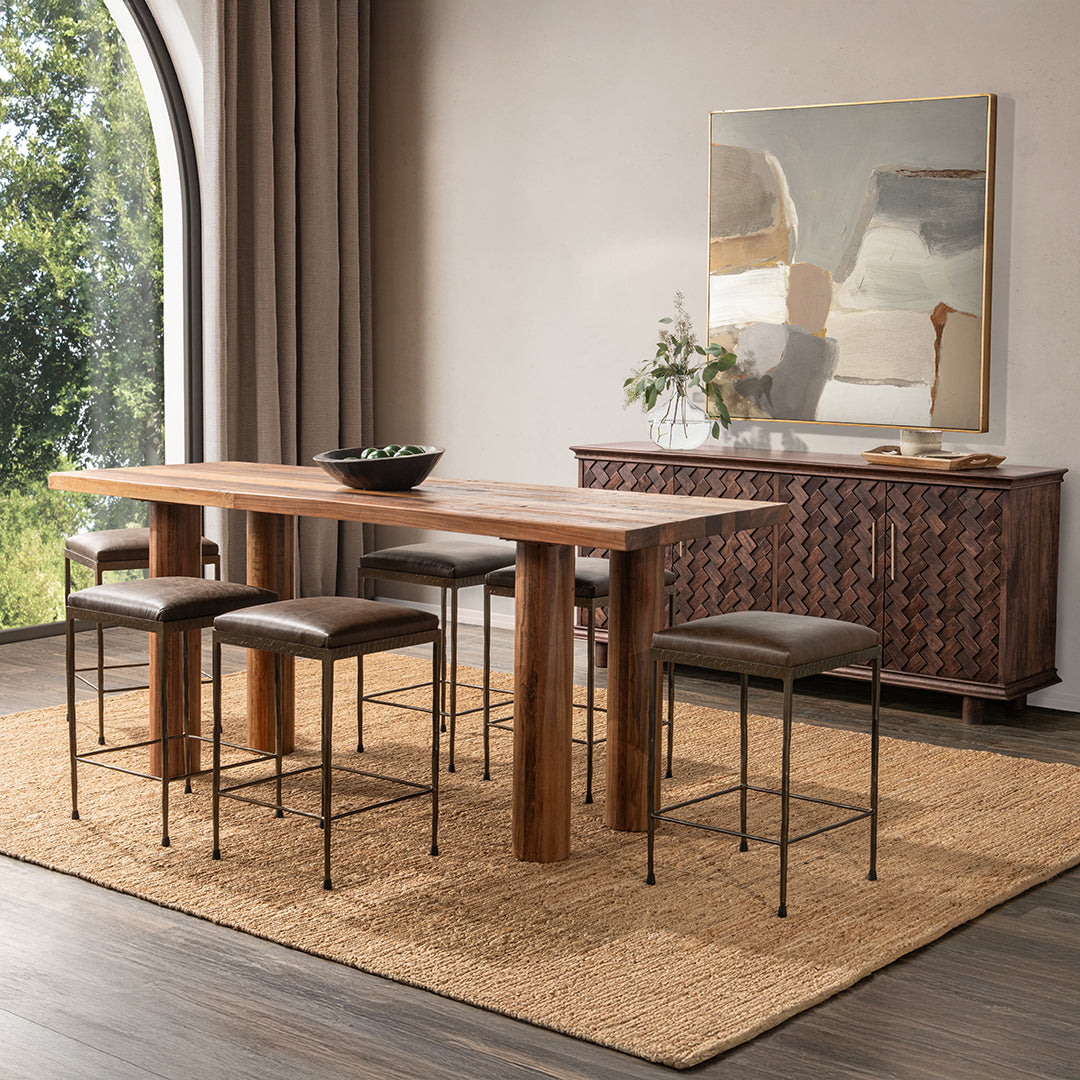 Dining area with wooden counter table and stools in a room with a large window and decorative wall art.