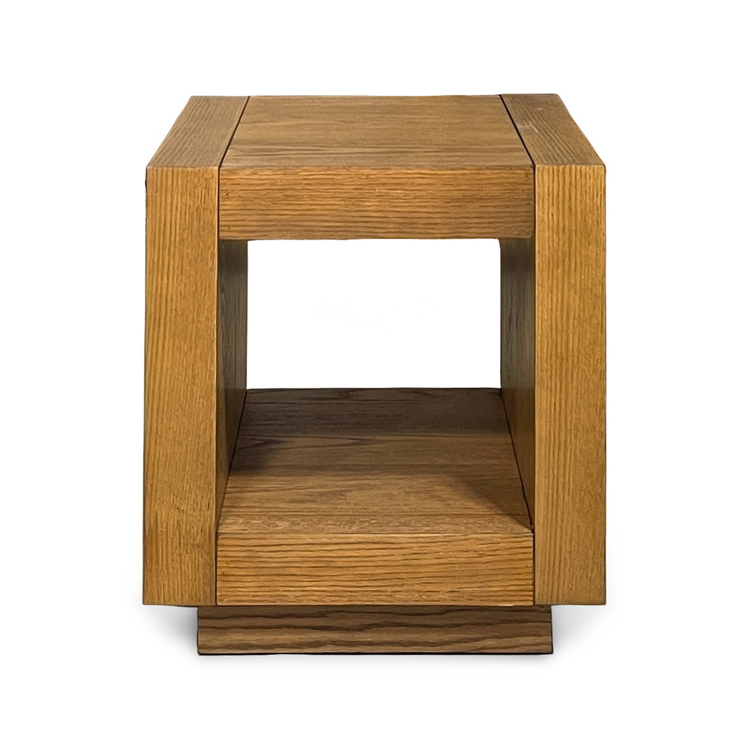 A square wooden end table with a geometric open-center design, featuring a top surface, a lower shelf, and a tiered base, crafted from oak wood with a warm golden-brown finish.