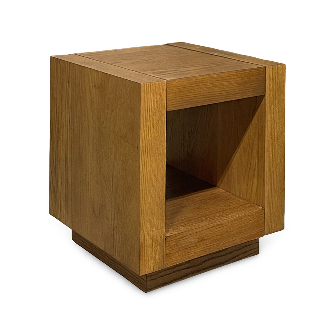 A modern geometric cube side table made of medium brown wood with a visible grain, featuring a single open cubby shelf.