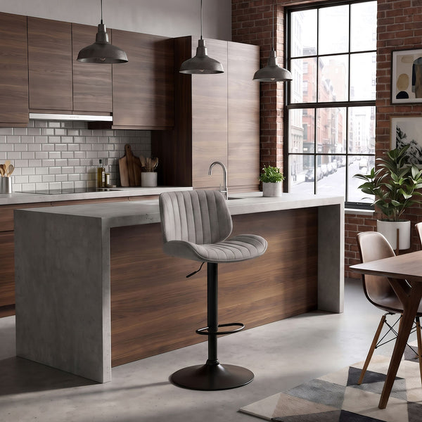 A modern kitchen island with a gray concrete-look base and a light gray ribbed upholstered swivel barstool with a black pedestal base, set in a contemporary kitchen with wood cabinets, brick walls, and pendant lights.