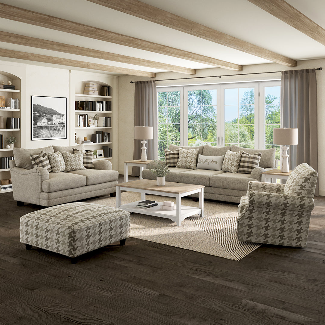 Modern living room with gray sectional sofa, armchair, and ottoman in a well-lit room with large windows.