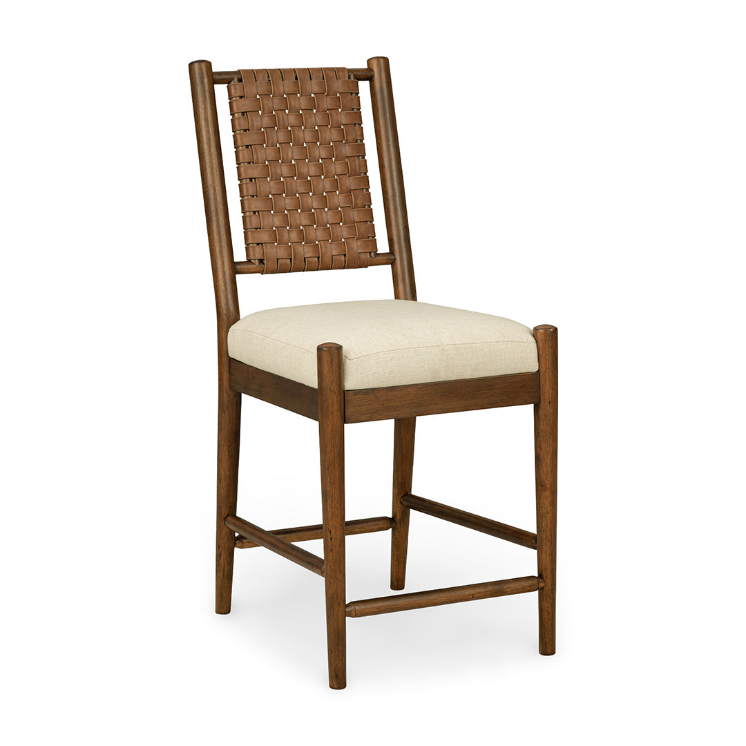 A wooden bar stool with a woven brown leather backrest, a cream-colored upholstered seat cushion, and a four-leg frame.