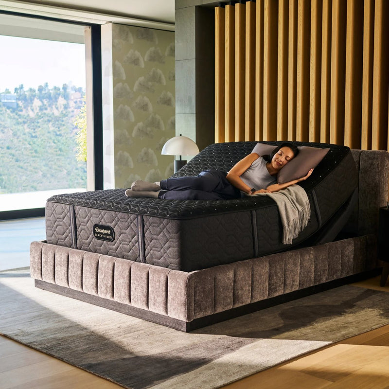 Woman sleeping on her side on a Beautyrest Black Hybrid mattress on an adjustable base in a modern bedroom with slatted wood wall feature and large window