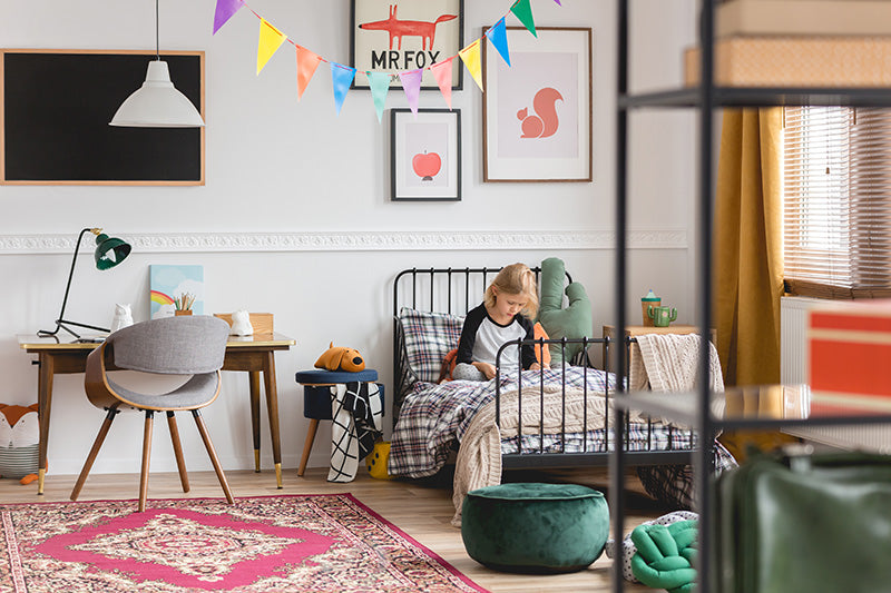 Child sitting on a twin bed in a bright kids bedroom with desk and colorful decor