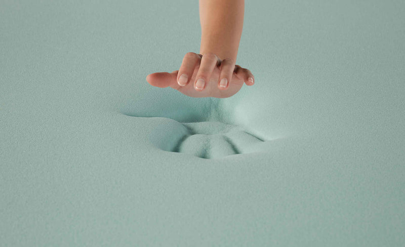 Hand pressing into dense light green memory foam, showing how the solid material molds to pressure