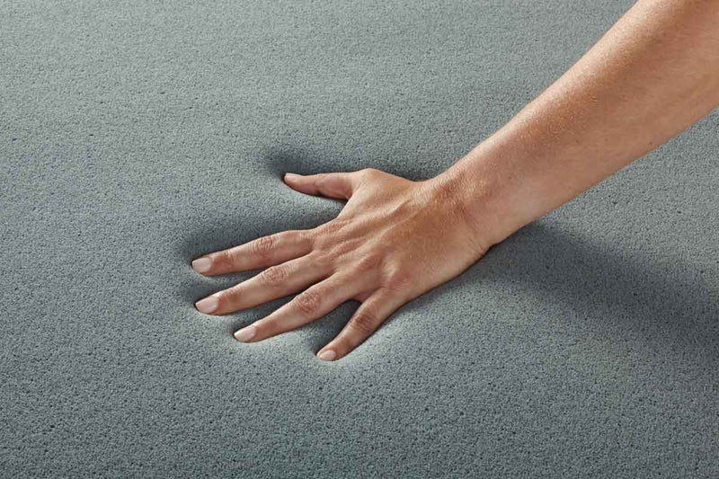 Close-up of a hand pressing into gray open-cell memory foam showing its porous structure