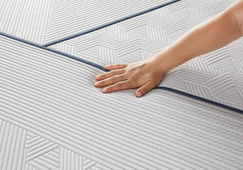 Close-up of a hand pressing on a quilted mattress cover with dark piping