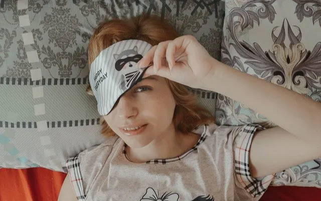 Woman resting in bed wearing a sleep mask on patterned pillows