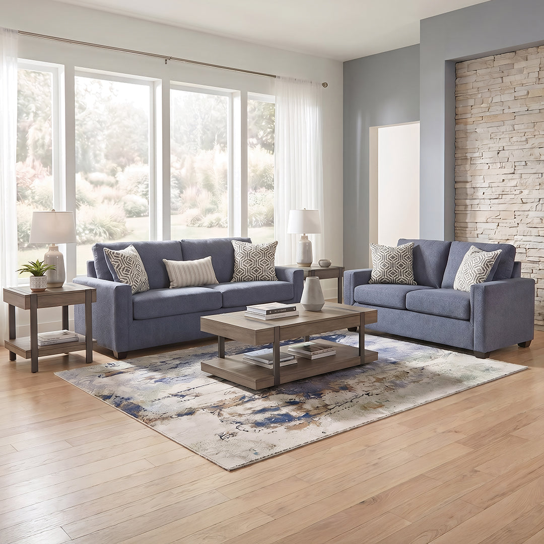 Properly sized living room area rug anchoring a blue sofa, loveseat, and coffee table layout on hardwood flooring