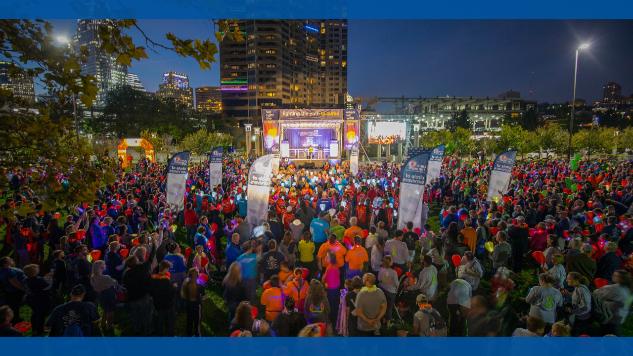 Crowd at an outdoor event, stage illuminated at night.