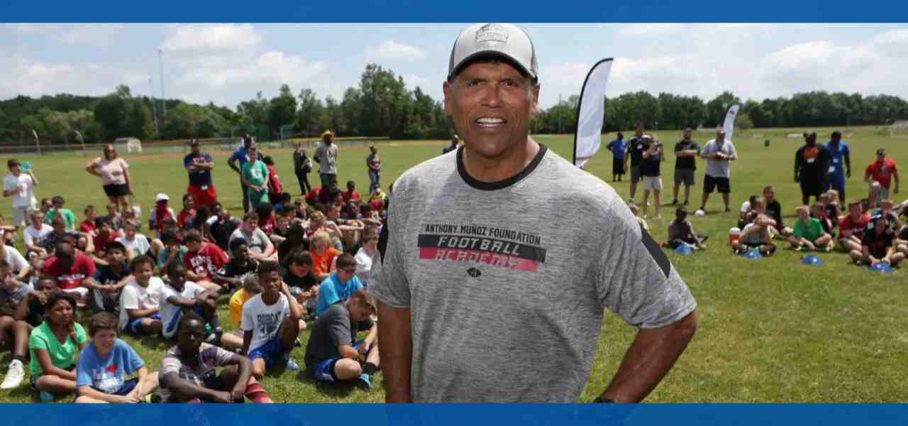 A man stands in front of a large group of children outdoors.