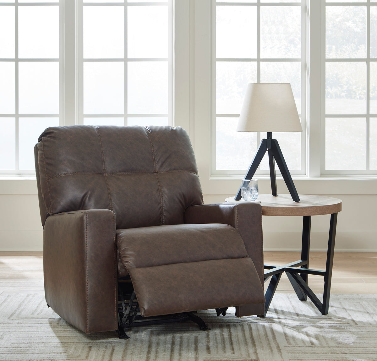 Brown leather recliner extended into full recline position beside an accent table and window in a home living room