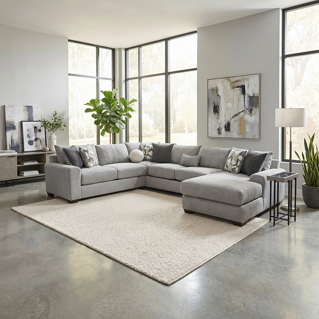 Modern living room with a gray sectional sofa, large windows, and decorative plants.
