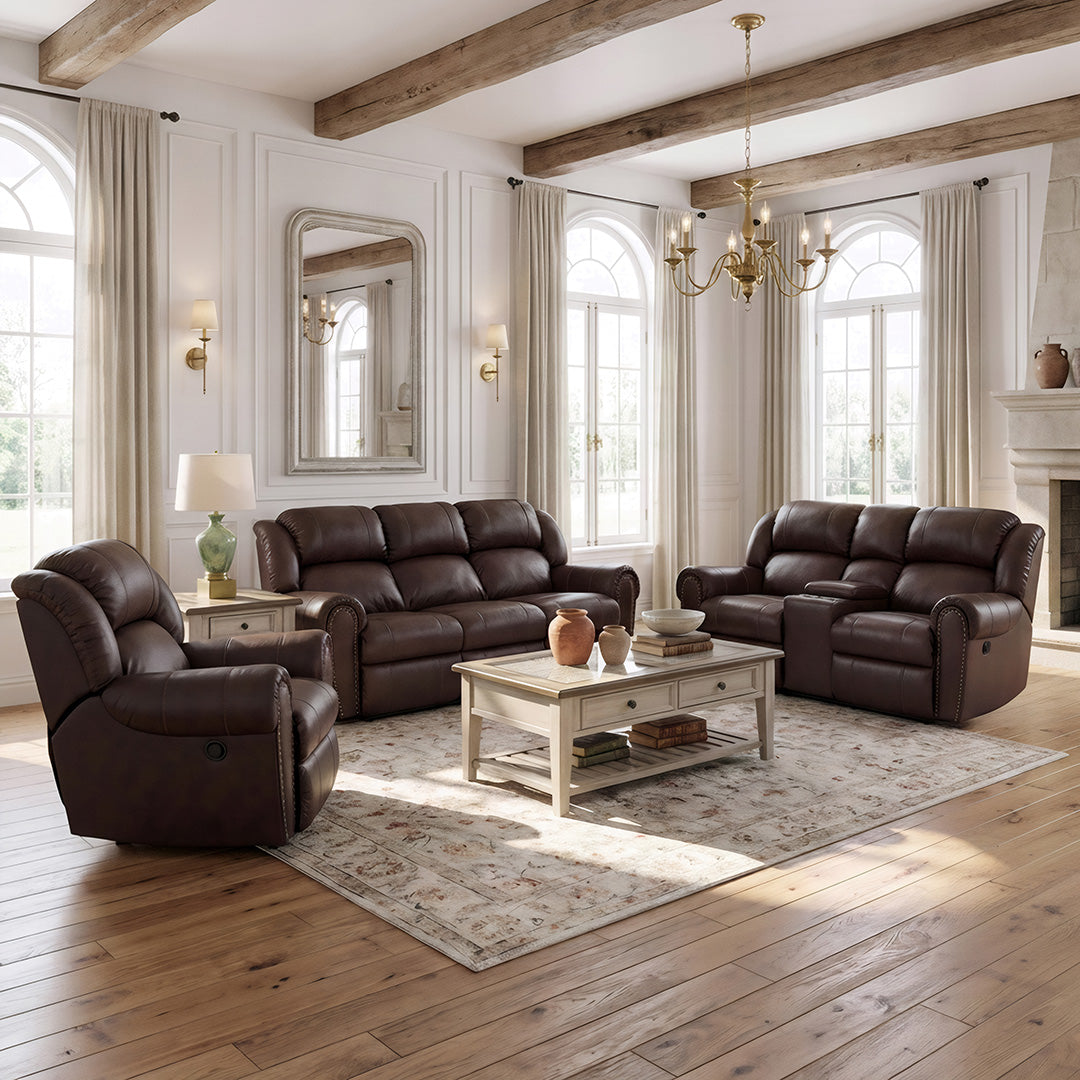 A staged living room showing a dark brown leather sofa, matching loveseat, and a dark brown leather recliner arranged around a white coffee table on a patterned area rug. The room features white walls, arched windows with beige curtains, a fireplace, and exposed wooden ceiling beams.