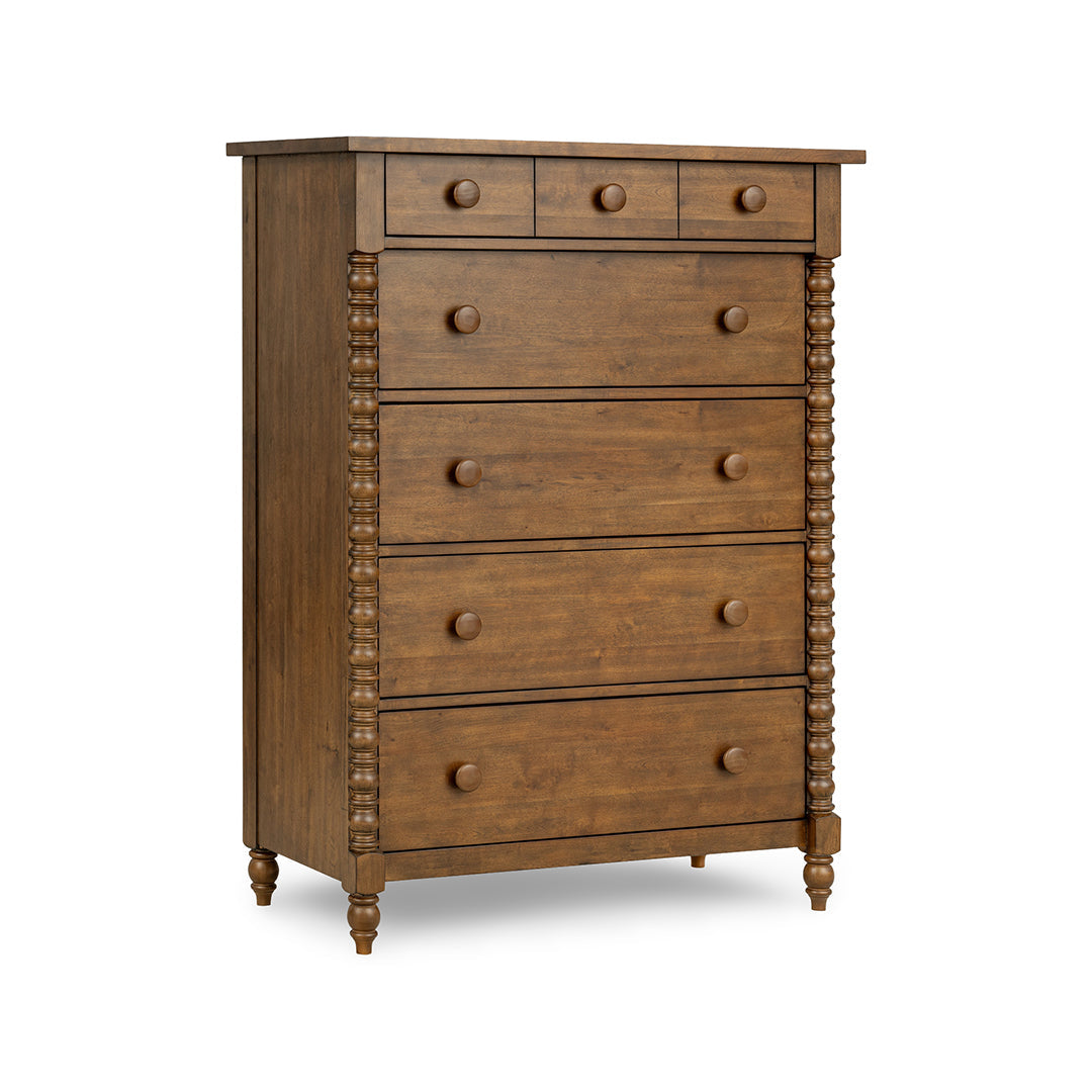 A five-drawer wooden chest of drawers with a medium brown finish, featuring decorative turned spindle posts on the sides and small round knobs on each drawer front.