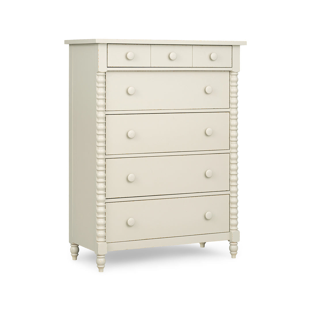 An off-white five-drawer chest of drawers with round knobs, turned legs, and decorative fluted side details.