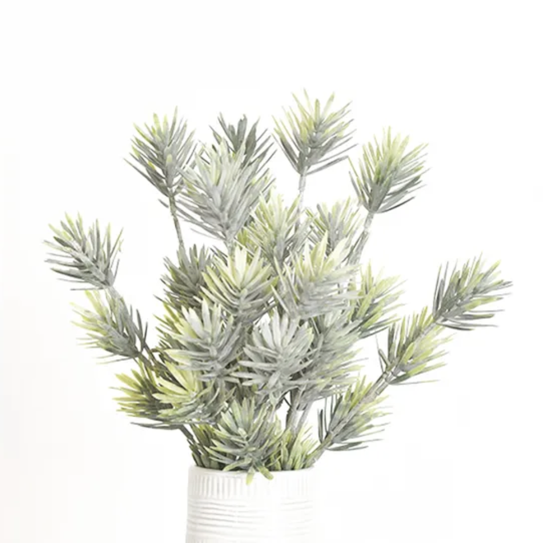 An artificial blue-green pine branch arrangement in a white ribbed pot, photographed against a seamless white background.