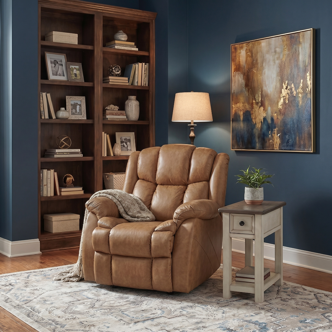 Brown leather recliner chair in a living room with bookshelf, lamp, and artwork.