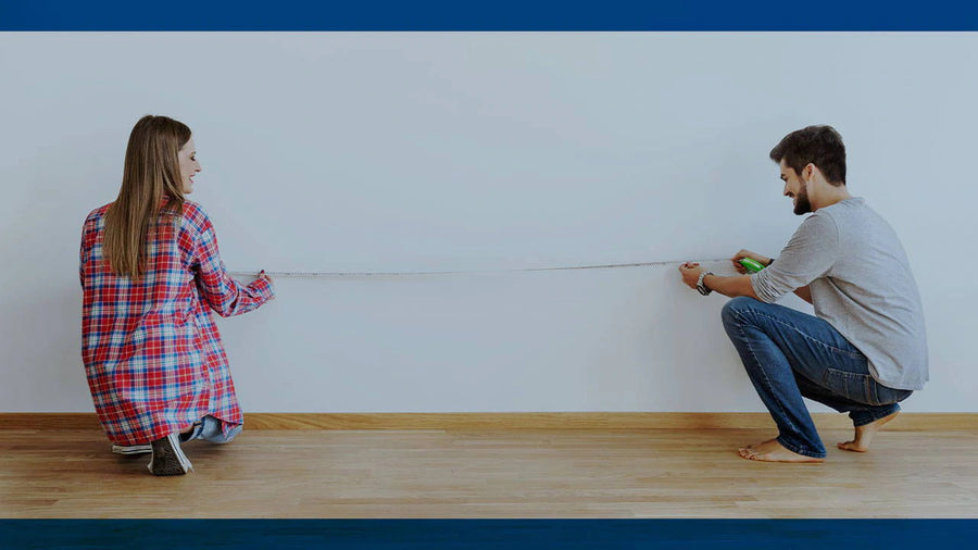 Homeowners taking room and floor measurements with a tape measure before buying living room furniture
