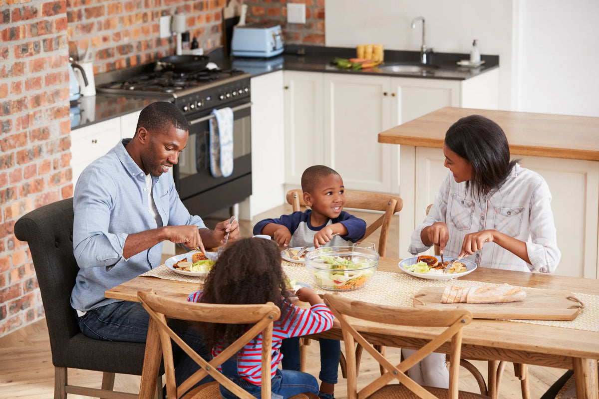 Family of four seated together enjoying dinner at a solid wood dining table in a kitchen dining area