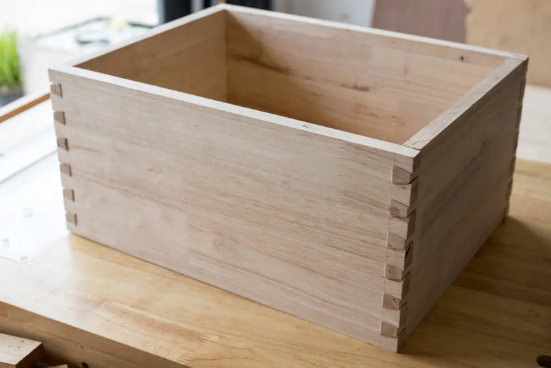 Unfinished wooden drawer box with visible dovetail joinery on a workbench