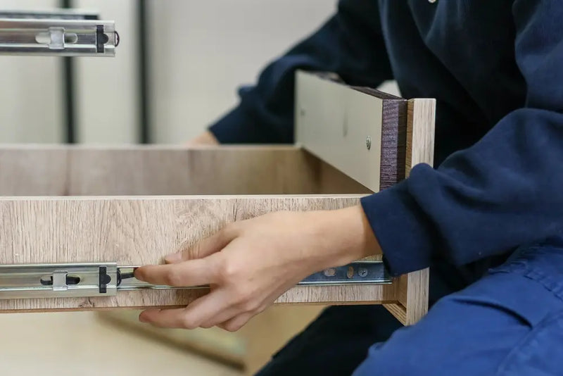 Person installing full-extension metal drawer slide rails inside a dresser