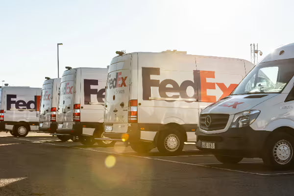 Row of white FedEx delivery vans parked in a lot representing third-party freight shipping