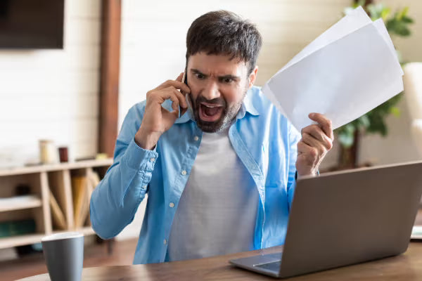 Frustrated man on the phone holding papers, representing difficulty resolving issues with remote customer service