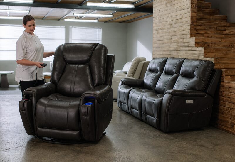 Furniture Fair sales team member demonstrating Moto Motion power recliner features with remote control in showroom