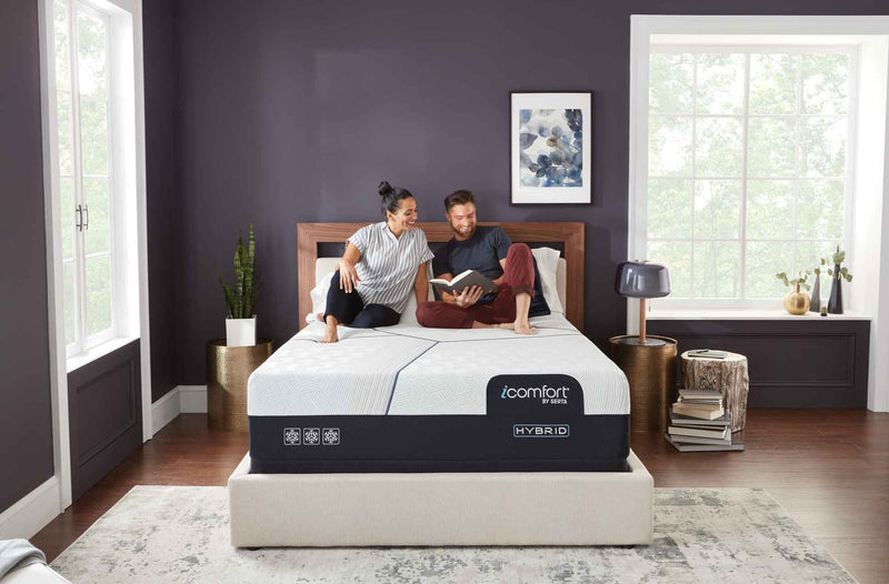 Couple reading together on an iComfort by Serta mattress in a bedroom with a wooden headboard