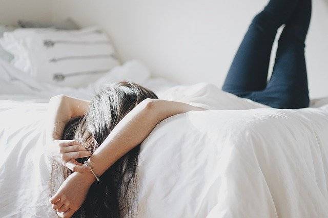 Person lying face-down across a white mattress, the sleeping position that puts the most strain on the lower back
