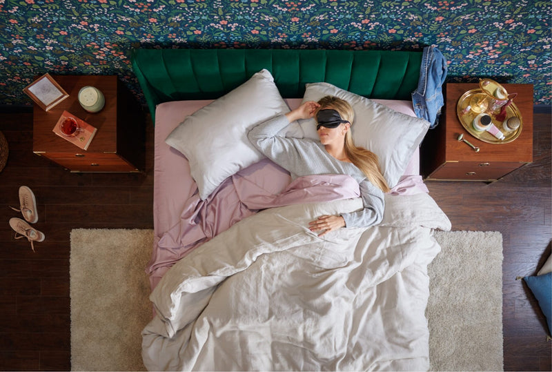 Woman sleeping peacefully on soft sheets and pillows in a styled bedroom