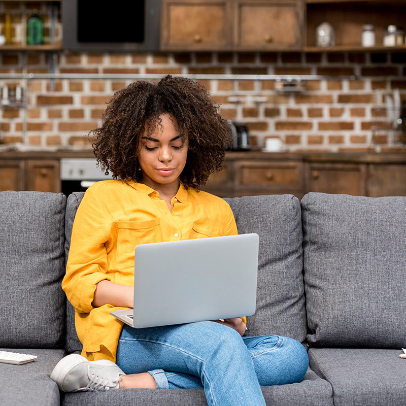 Young college student relaxing on a gray sofa with a laptop in a modern apartment
